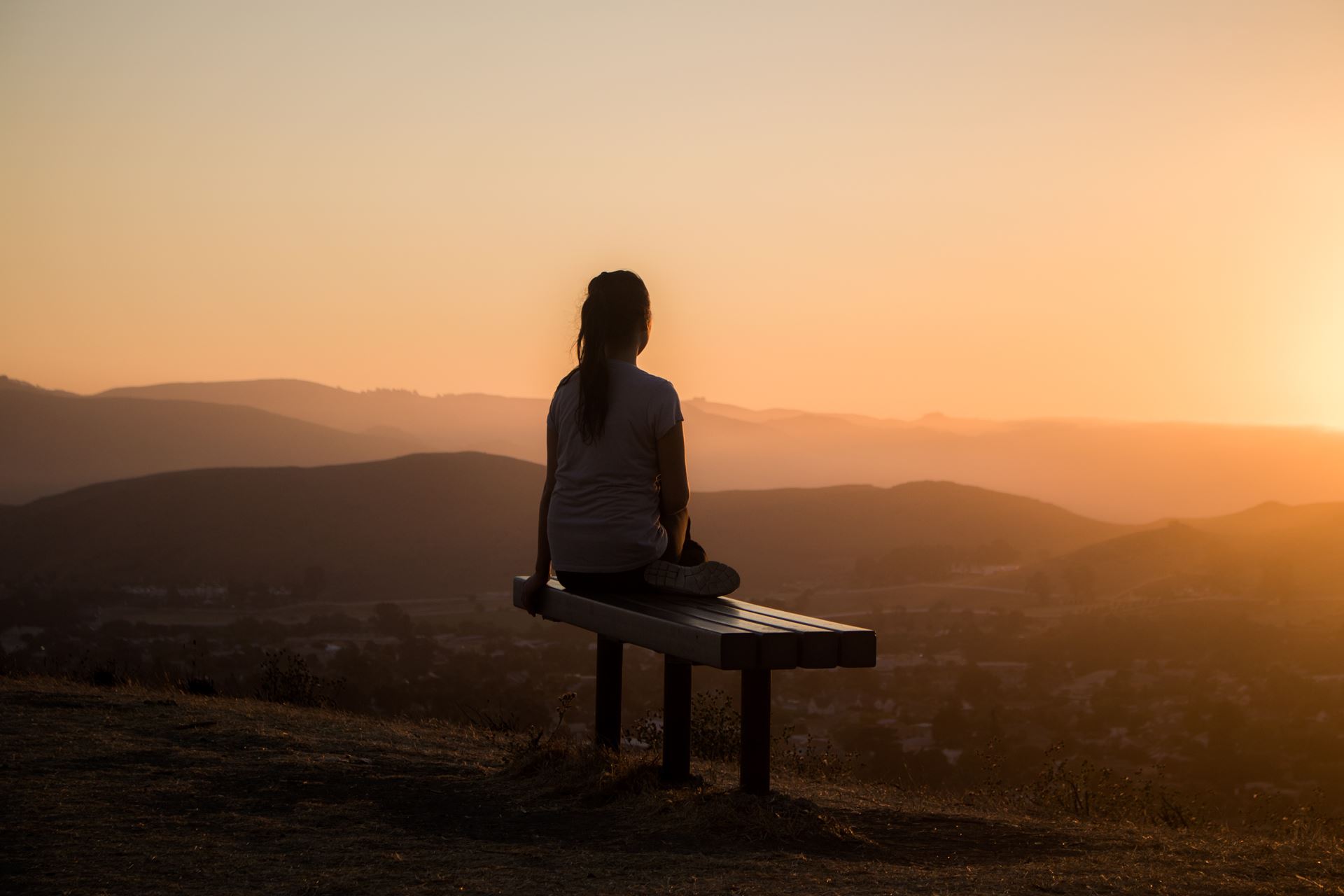 a person sitting on a bench in front of a sunset